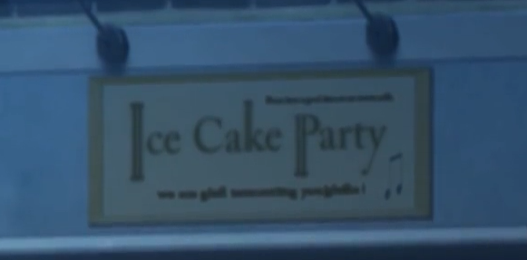 A monochrome yellow sign reading 'Ice Cake Party'. The I, K, and P are elongated. Above and below this is much smaller indiscernable text and a music note.