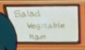 A sign or possibly a whiteboard, reading 'Salad Vegetable Ham'. Each word is on a new line, and 'vegetable' is misspelled, making the second E an I.